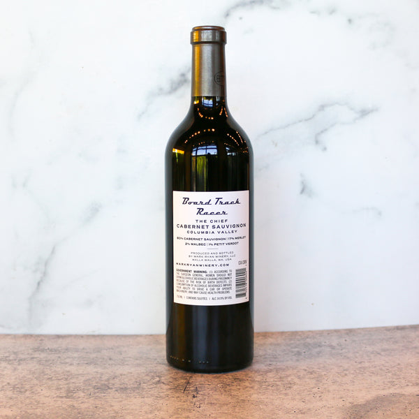 Wine bottle, showing the back,  labeled 'Board Track Racer' on a wooden surface with a marble background, A bottle is available at TASTE across costal Virginia and Richmond and online at TASTE.online