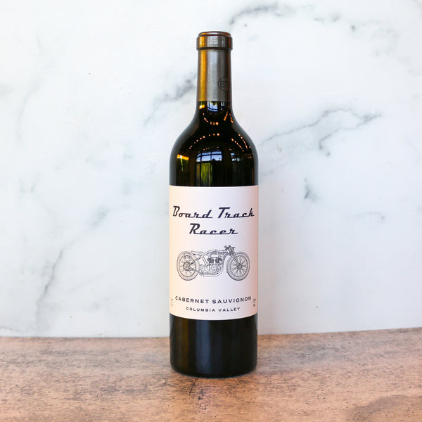 Wine bottle labeled 'Board Track Racer' on a wooden surface with a marble background, A bottle is available at TASTE across costal Virginia and Richmond and online at TASTE.online