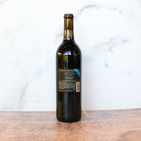 A bottle of CHRIS HAMILTON NAPA RED Blend available at TASTE across costal Virginia and Richmond and online at TASTE.online - Wine bottle with a blue label on a wooden surface and marble background