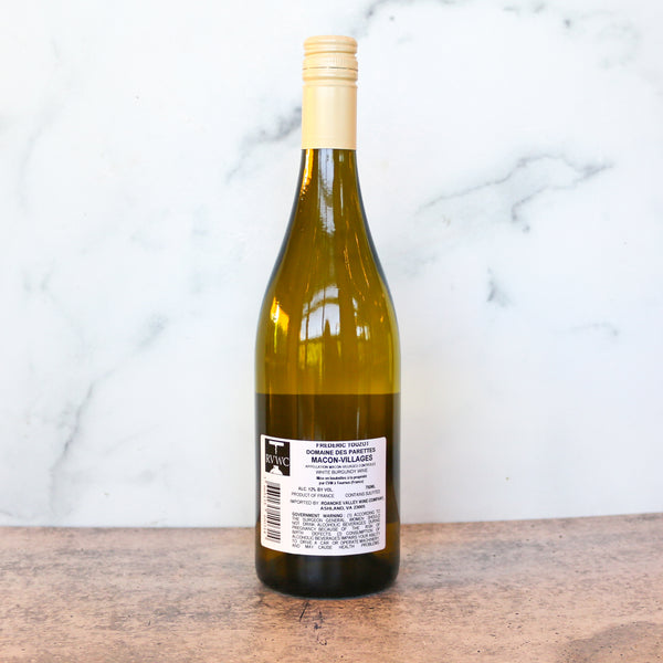 A bottle of DOMAINE DES PARETTES MACON-VILLAGES CHARDONNAY available at TASTE across costal Virginia and Richmond and online at TASTE.online on a wooden surface with a marble background. Wine bottle with a label on a wooden surface and marble background