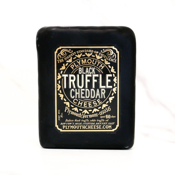 Black truffle cheddar cheese bar with gold label on a white background