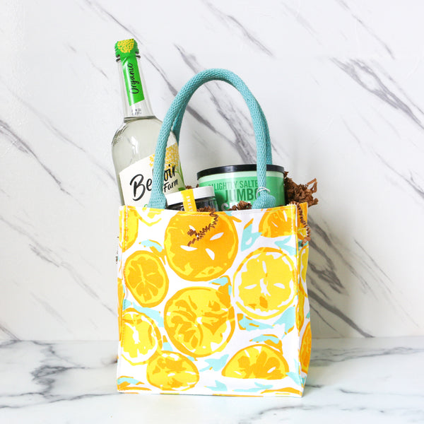 Fabric basket with lemon pattern containing a bottle and a can on a marble surface