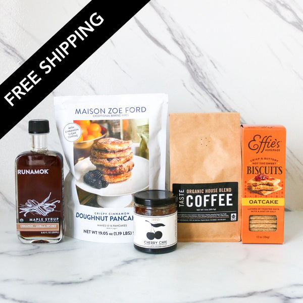 Assorted food products including a bottle of Runamok maple syrup, a bag of Maison Zoe Ford doughnut pancake mix, a jar of Cherry Chin jam, a box of Effies biscuits, and a bag of Taste Organic House Blend coffee on a marble surface with 'Free Shipping' text overlay.