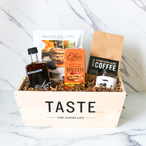 TASTE Gift basket labeled 'Taste the Good Life' with coffee, biscuits, and other items on a marble surface.