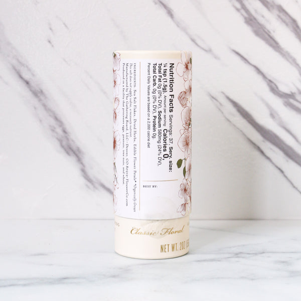 Flower co. garnishing salt with classic floral pattern, displaying nutrition facts and ingredients, cylindrical packaging on a marble background