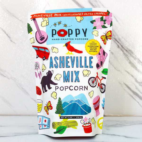 Colorful popcorn bag with 'Poppy' branding and 'Asheville Mix' design on a white marble background. 