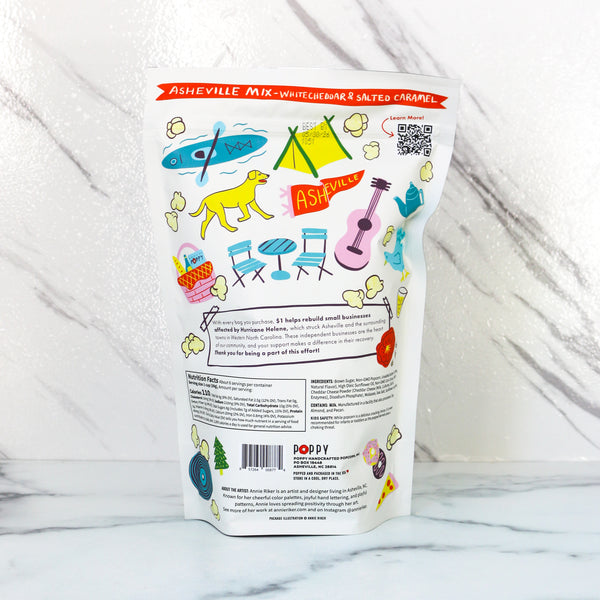 Colorful snack bag with illustrations on a marble surface. Poppy Asheville mix a mix of Car. 1$ from each sale helps rebuild small businesses affected by hurricane Helene