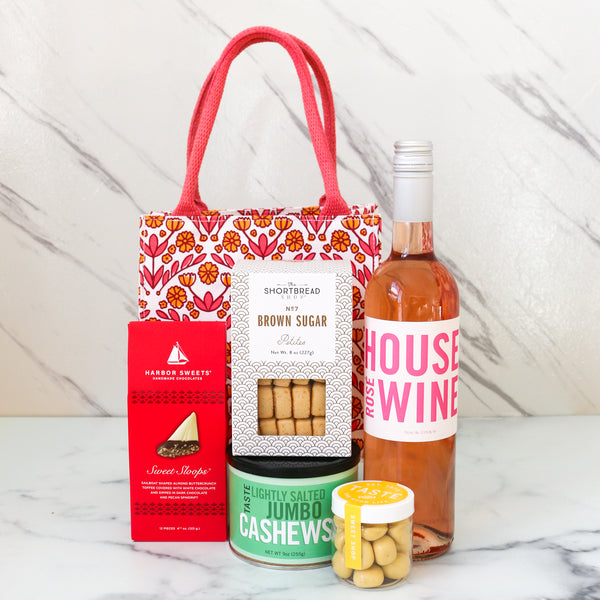 TASTE.online Gift set with a bottle of TASTE House Rose wine, cookies, and nuts on a marble surface with a striking pink and yellow Gift Bag
