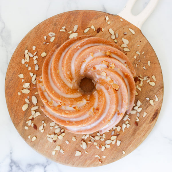 TASET Bakehouse Bundt cake on a wooden board with almonds, on a marble background