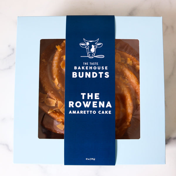  The Rowena Amaretto Cake Bundt cake packaging with 'The Taste Bakehouse' branding on a marble surface