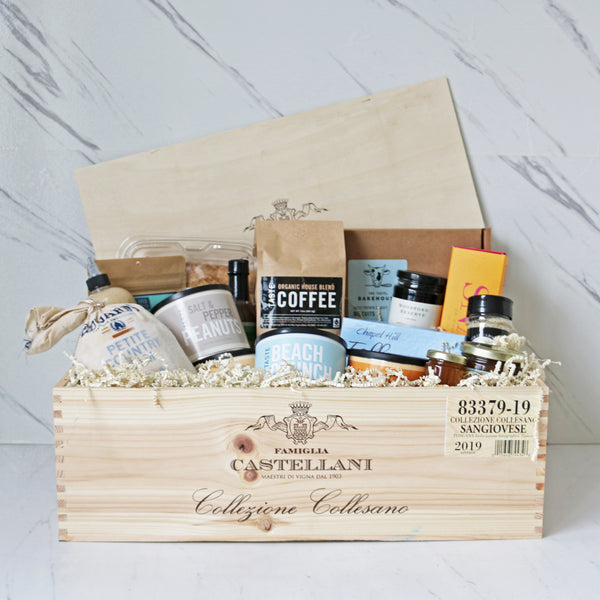A wooden crate filled with various food items including packages of biscuits, chocolates, nuts, and condiments, with a focus on products from Virginia.