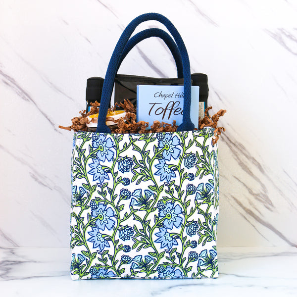 TASTE Gifts A Lil Something, all packed up and ready to give. One of TASTE's amazing gifts Assorted snacks and drinks including pretzels, two bottles of prosecco, and peanuts in a decorative bag on a white background.