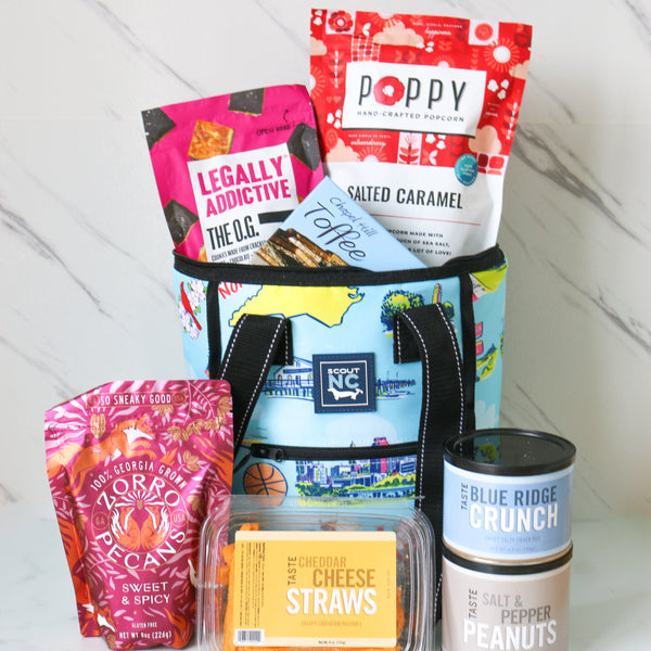 Insulated SCOUT North Carolina bag with assorted snack items including bags of chips and a container of cheese straws on a white marble  surface.