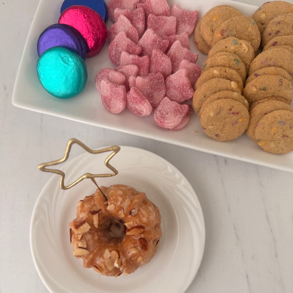 Assorted cookies and a star shaped sparkler on a white plate with a star-shaped holder on a white surface.