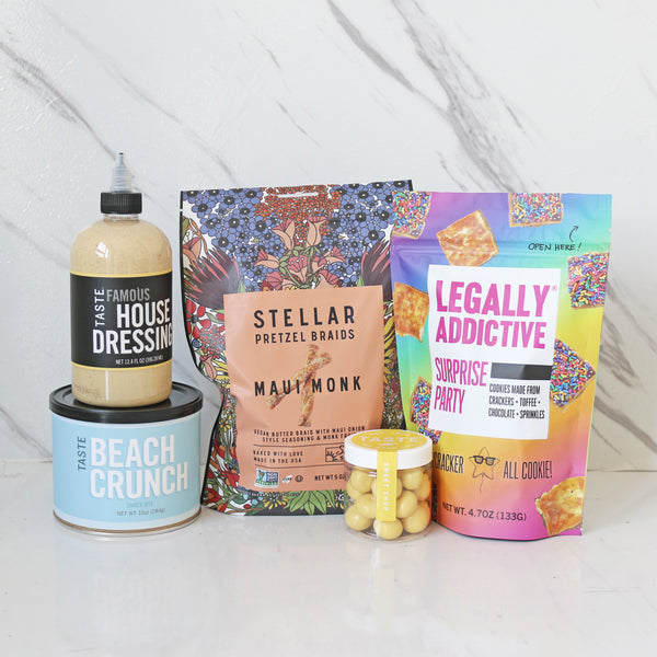 An assortment of food products from TASTE, including a can of nuts, a bottle of dressing, a packet of pretzels, a can of house dressing, and two other snack packages.