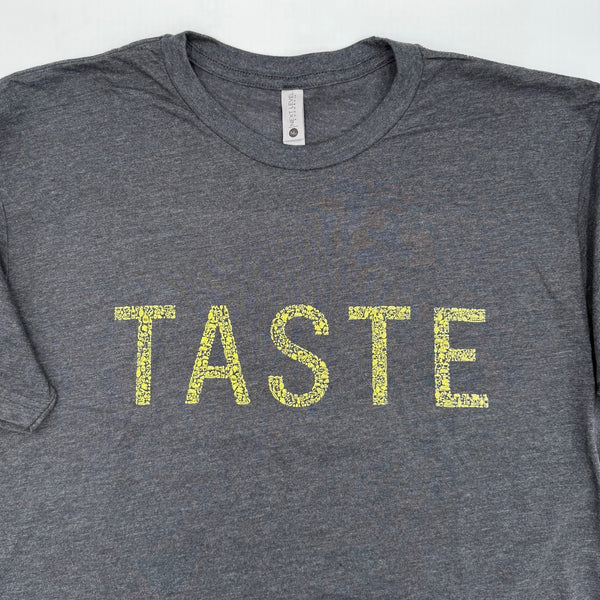 Gray t-shirt with 'TASTE' printed in yellow on a white background