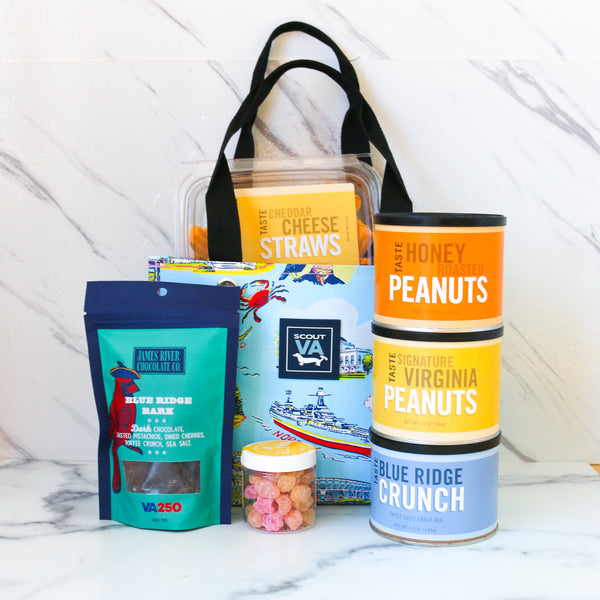 Assorted food products including a Cans of Virginia peanuts, a container of TASTE cheese straws, and jars on a marble surface, all packed in a SCOUT tiny package bag.