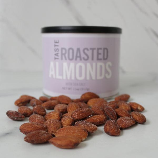 A can of TASTE Roasted Almonds with some almonds scattered in front, on a marble surface.