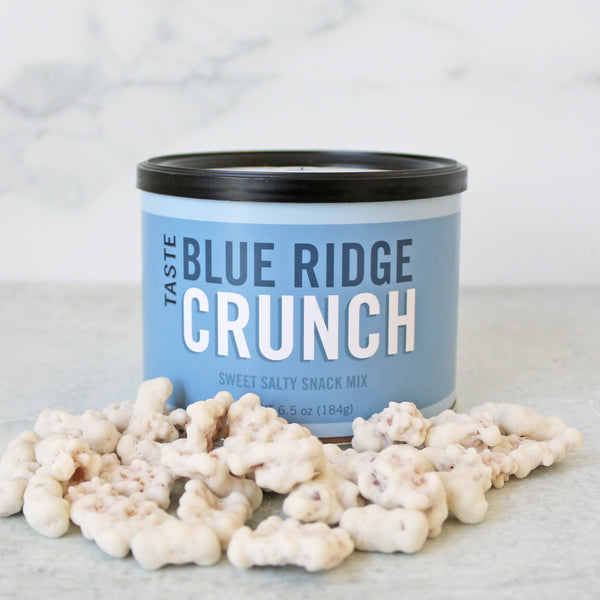 A can of TASTE Blue Ridge Crunch sweet salty snack mix, with pretzels, oat cereal, graham cereal displayed in front.