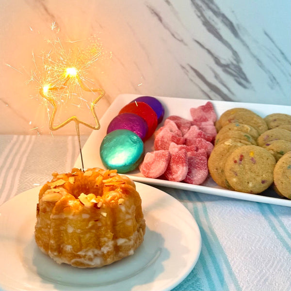 TASTE Bakehouse Baby Bundt cake with the star shaped sparkler, cookies on a marble surface.