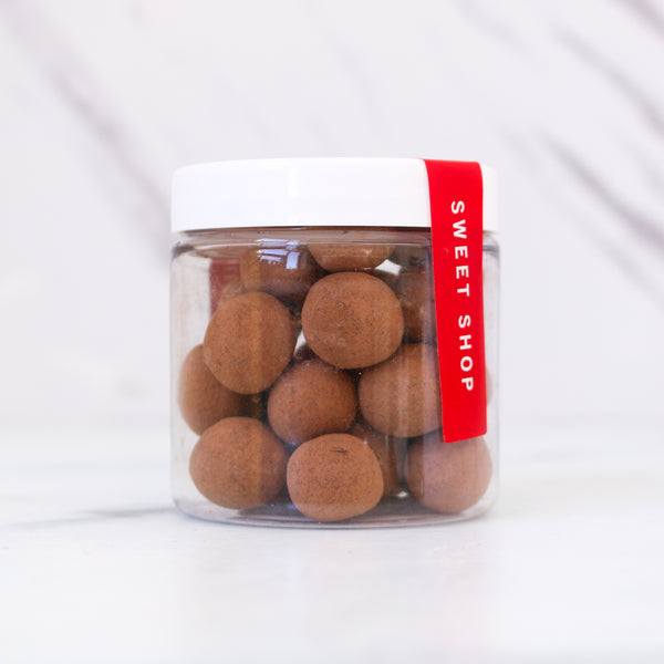 Jar of round brown candies with a red TASTE 'Sweet Shop' label on a white marble background