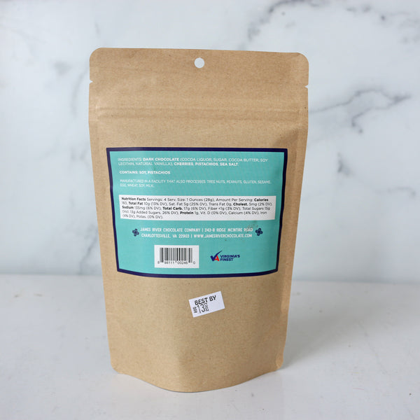 A packaged product labeled 'Blue Ridge Bark' by James River Chocolate Co., visible through a window on a brown paper bag, set against a marble background.