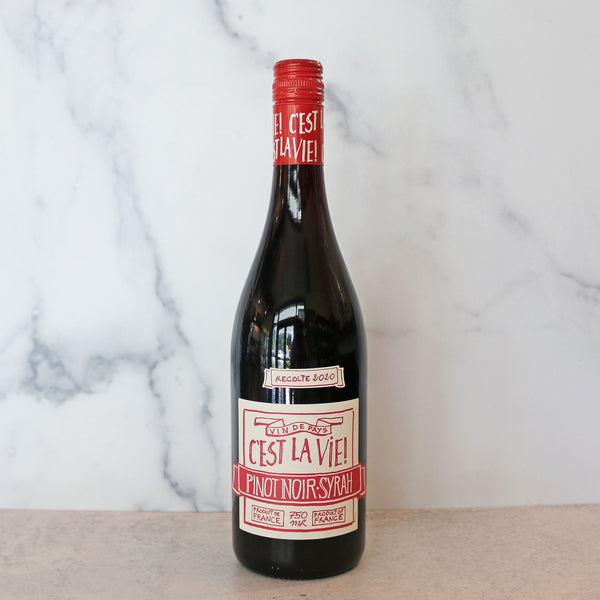 A bottle of C'est La Vie Pinot Noir - Syrah red wine with a label, placed on a marble surface.
