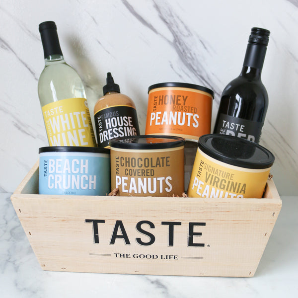 Basket of TASTE Branded snacks and red and white wine with labeled containers on a marble surface, featuring the brand 'Taste'.