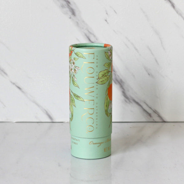 A cylindrical container with a green label featuring 'FLOUER CO. ORANGE BLOSSOM' text, indicating it contains cocktail cubes infused with orange blossom.
