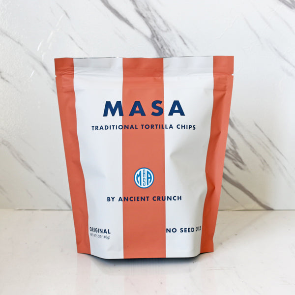 A bag of MASA Traditional Tortilla Chips by Ancient Crunch, with a predominantly white and orange color scheme, indicating that the product is gluten-free and non-GMO.