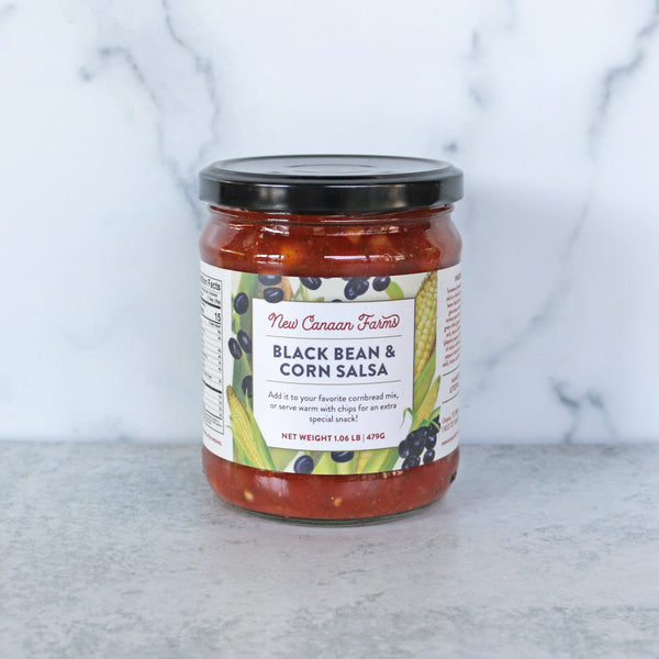 A jar of New Canaan Farms Black Bean & Corn Salsa on a marble surface.