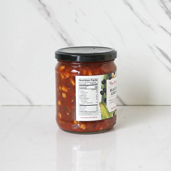 A jar of New Canaan Farms Black Bean & Corn Salsa on a marble surface, showing nutrition facts