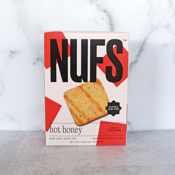 A box of Nufs Gluten-Free Crackers - Hot Honey flavor, with the product visible on the front. The background is marble.
