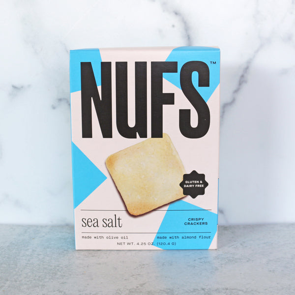 A box of Nufs gluten-free crackers with sea salt. The packaging is predominantly white with blue accents and an image of the crackers.