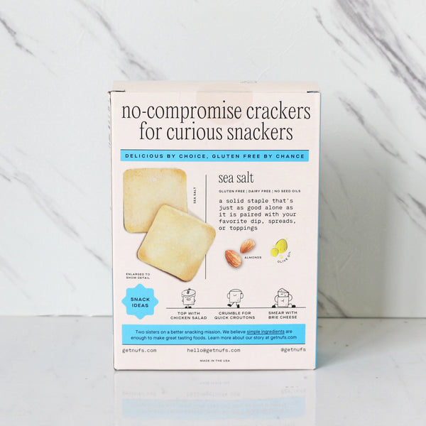 A box of Nufs gluten-free crackers with sea salt. The packaging is predominantly white with blue accents and an image of the crackers.
