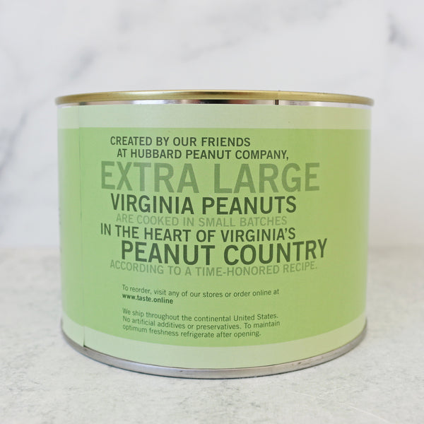 A green cylindrical tin labeled 'SALT FREE VIRGINIA PEANUTS' with a pile of raw peanuts in front of it on a marble surface.