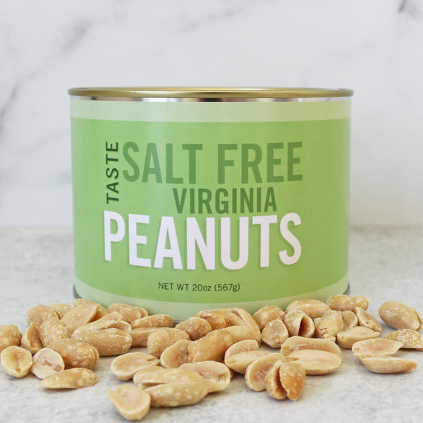 A green cylindrical tin labeled 'SALT FREE VIRGINIA PEANUTS' with a pile of raw peanuts in front of it on a marble surface.