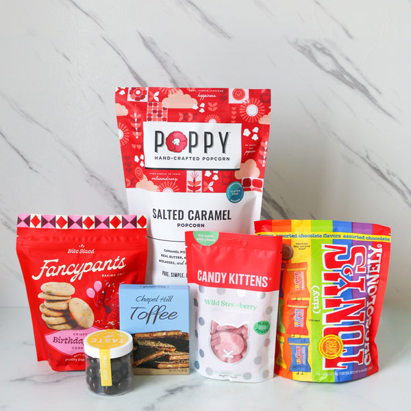 Assorted snack packages including Poppy, Fancypants, and Choc-tilly on a marble surface.
