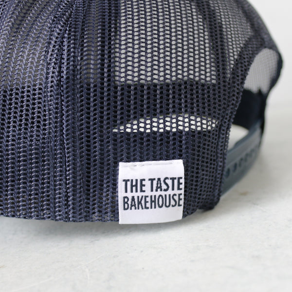 Navy blue trucker hat with the iconic TASTE Bakehouse cow logo on a light gray background featuring a close-up Rear tag 