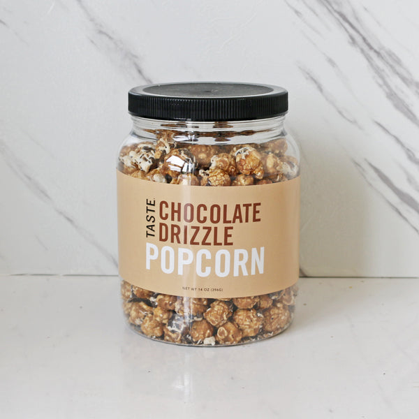 A clear jar filled with caramel popcorn drizzled with white and dark chocolate, labeled 'TASTE Chocolate Drizzle Popcorn'.