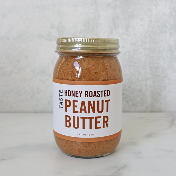 A jar of TASTE Honey Roasted Peanut Butter on a marble surface.