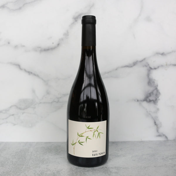 A bottle of Abiouness Ten Rows Carneros Pinot Noir wine positioned in front of a marble background.