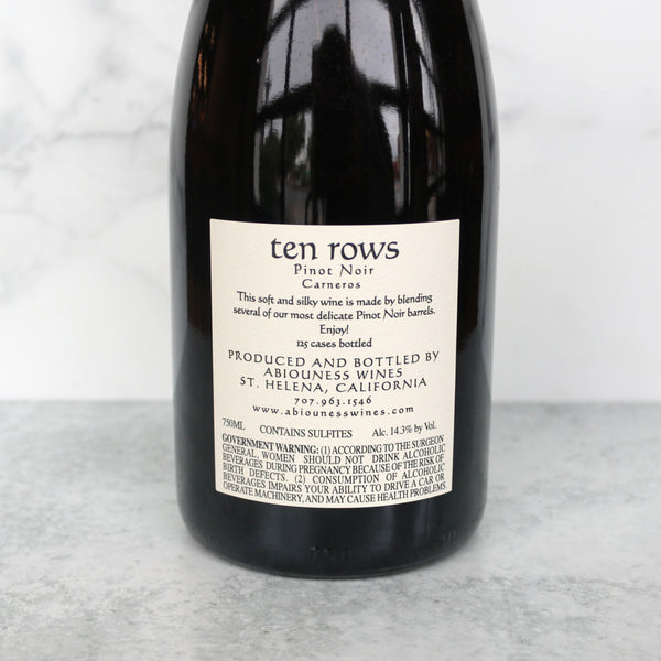 back of a  bottle of Abiouness Ten Rows Carneros Pinot Noir wine positioned in front of a marble background.