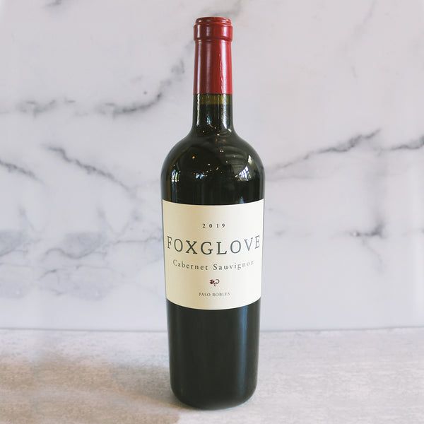A bottle of Foxglove Cabernet Sauvignon with a label that includes the wine variety and the brand name. The bottle is upright and has a red cap, set against a marble background.