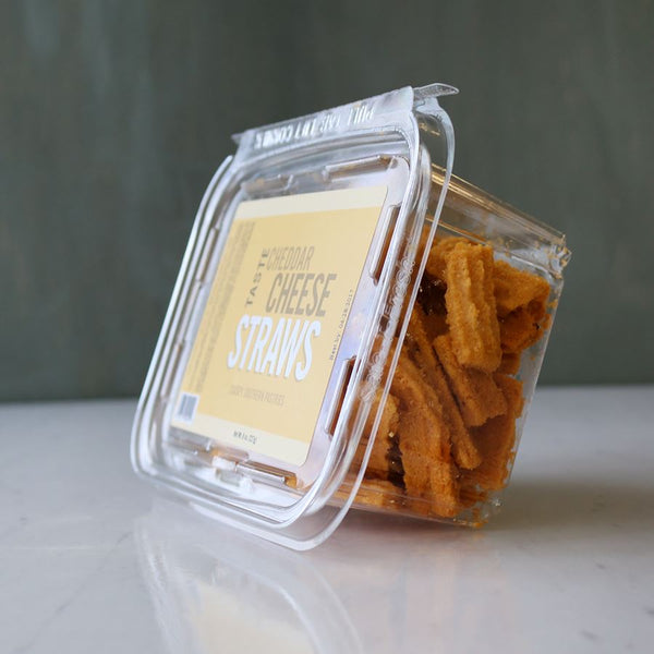 A resealable plastic container of TASTE Cheddar Cheese Straws on a marble surface.