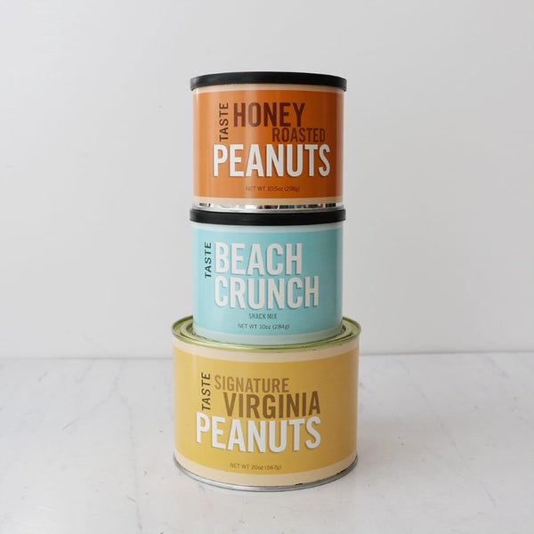 Three stacked cans of TASTE brand snacks, with labels indicating Honey Roasted Peanuts, Beach Crunch Snack Mix, and Signature Virginia Peanuts.