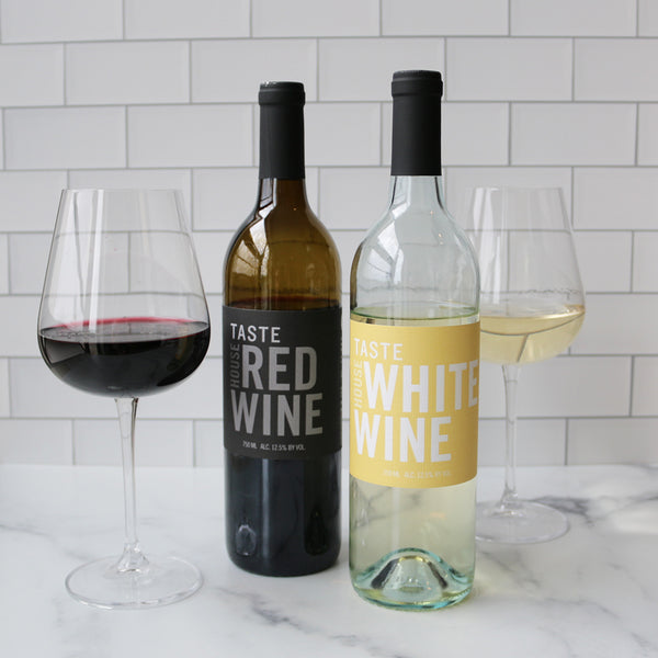 Two bottles of wine, one labeled TASTE RED WINE and the other TASTE WHITE WINE, with a clear glass in the foreground filled with red wine.