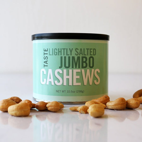 A can of TASTE Lightly Salted Jumbo Cashews with several cashew nuts scattered in front, against a light background.
