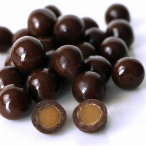 dark chocolate sea salt caramels from TASTE Sweet Shop on a grey surface, with some candies spilling out on a table