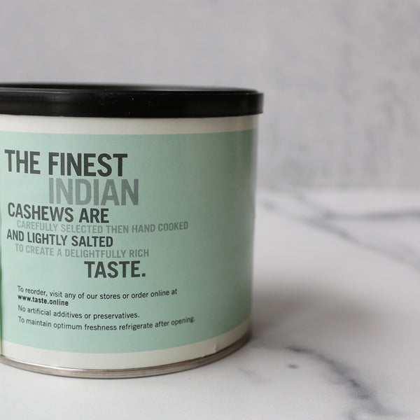 A can of TASTE Lightly Salted Jumbo Cashews with several cashew nuts scattered in front, against a light background.